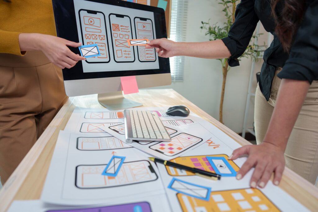 Two female web designers are discussing the user interface and user experience of a mobile app, comp